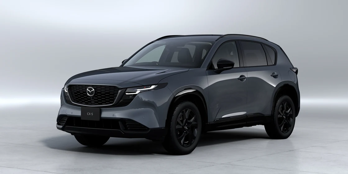 濃い灰色の新型CX-5を左斜め前から見た外観。明るいスタジオの背景に、黒いホイールと細いヘッドライトが見える