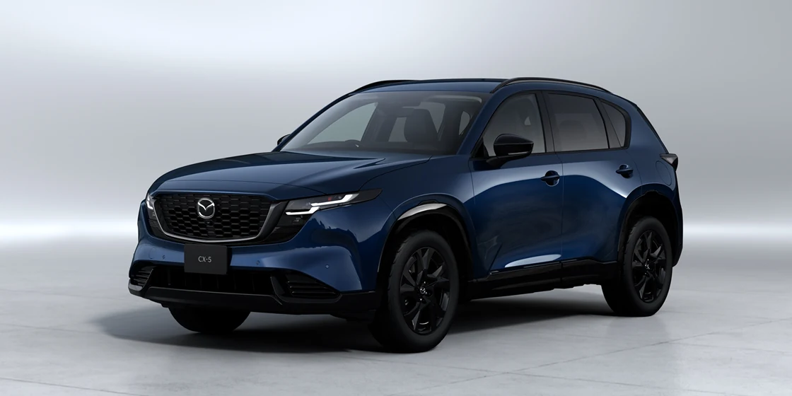 青い新型CX-5を左斜め前から見た外観。明るいスタジオの背景に、黒いグリルと黒いホイールが見える