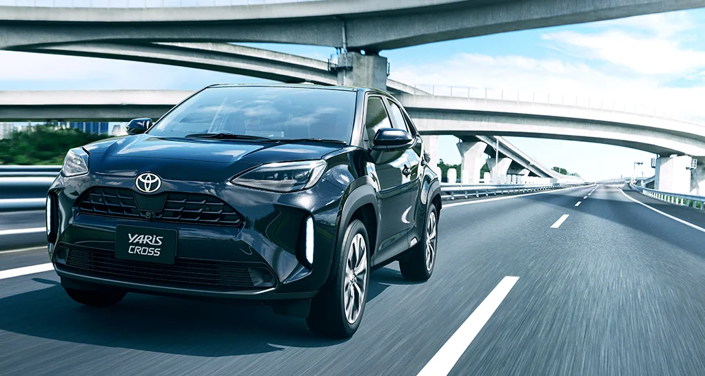 高架の下の道路を走る黒いヤリス クロスの前面。ヘッドランプとフロントグリルが見える