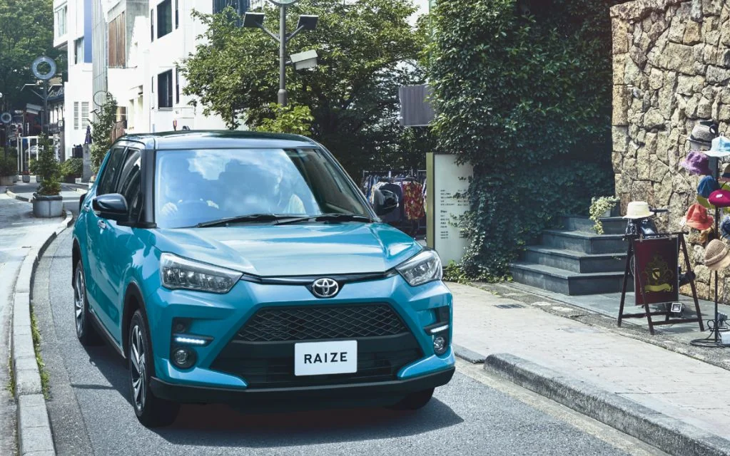 街なかの道にいる青いトヨタ ライズの前面。フロントグリルとヘッドランプ、ナンバー位置のRAIZEのプレートが見える