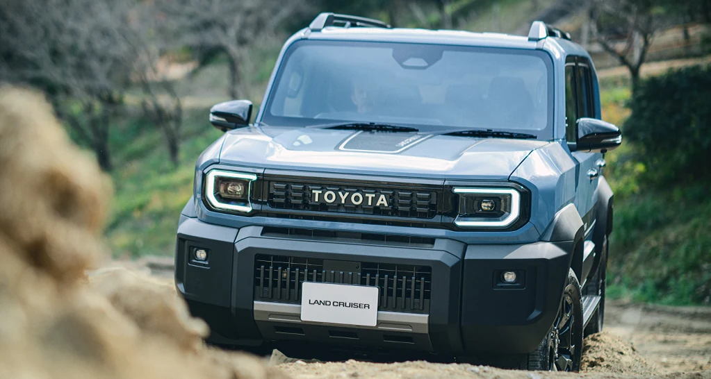 ランドクルーザーFJを、砂地の悪路で正面から見た外観。角目のヘッドランプとTOYOTAのロゴが付いたフロントが見える