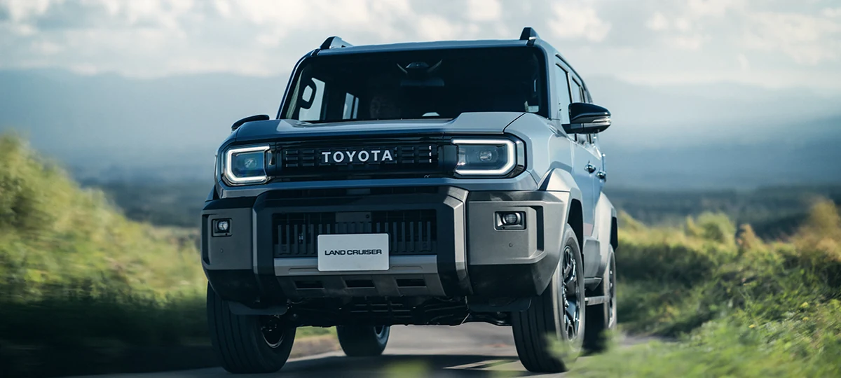 緑に囲まれた道を走るランドクルーザーFJを、正面から見た外観。丸い縁取りのヘッドランプとTOYOTAのロゴが見える