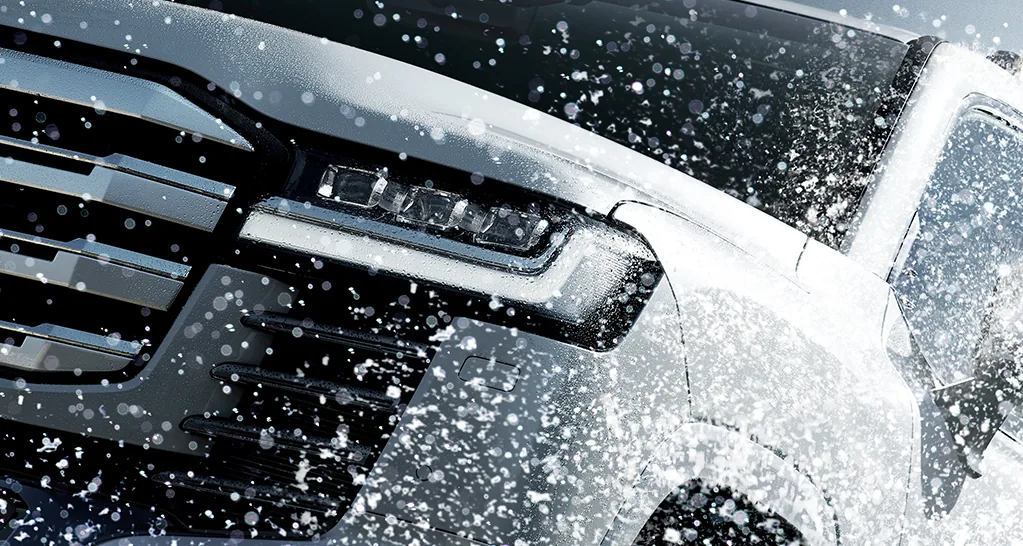 雪が吹きつけるランドクルーザー300のフロントまわりのアップ。左にグリルの一部、中央にLEDのヘッドランプが見える