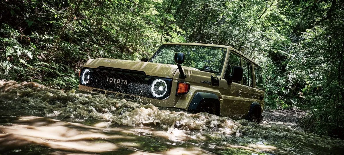 森の中の川を水しぶきを上げて進むランドクルーザー70の外観。フロントグリルの「TOYOTA」の文字と丸いヘッドランプが見える