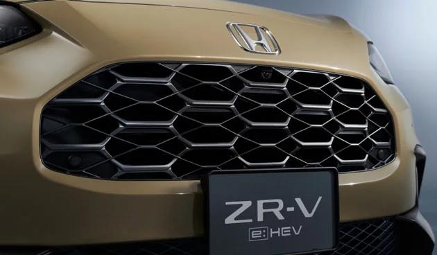ベージュのZR-Vの前を近くから見た写真。六角形を重ねたグリルと、その上のHマーク、下のZR-V e:HEVの板が写る