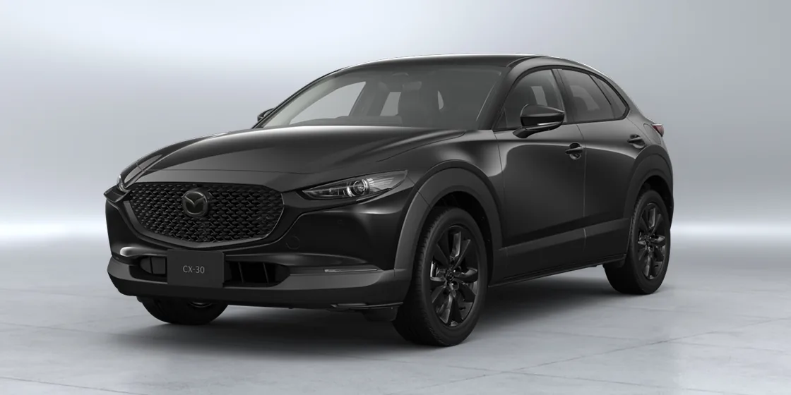 明るいスタジオに置いた黒いCX-30を左斜め前から見た外観。黒いメッシュのグリルと黒いホイールが分かる