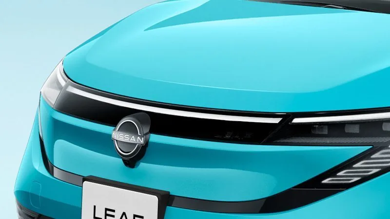3代目の日産リーフのフロントの接写。ターコイズのボンネットの先に、細く光る横一文字のランプと日産のエンブレムが並ぶ