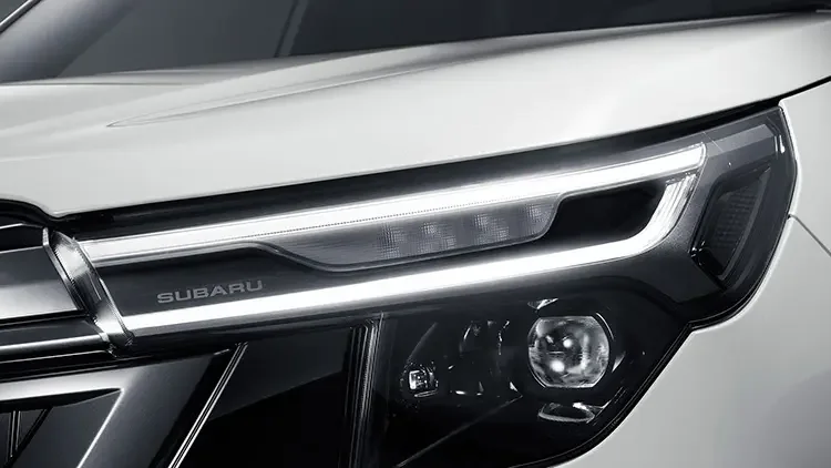 白いフォレスターの前側。細長いヘッドライトと、その下のSUBARUの文字が見える