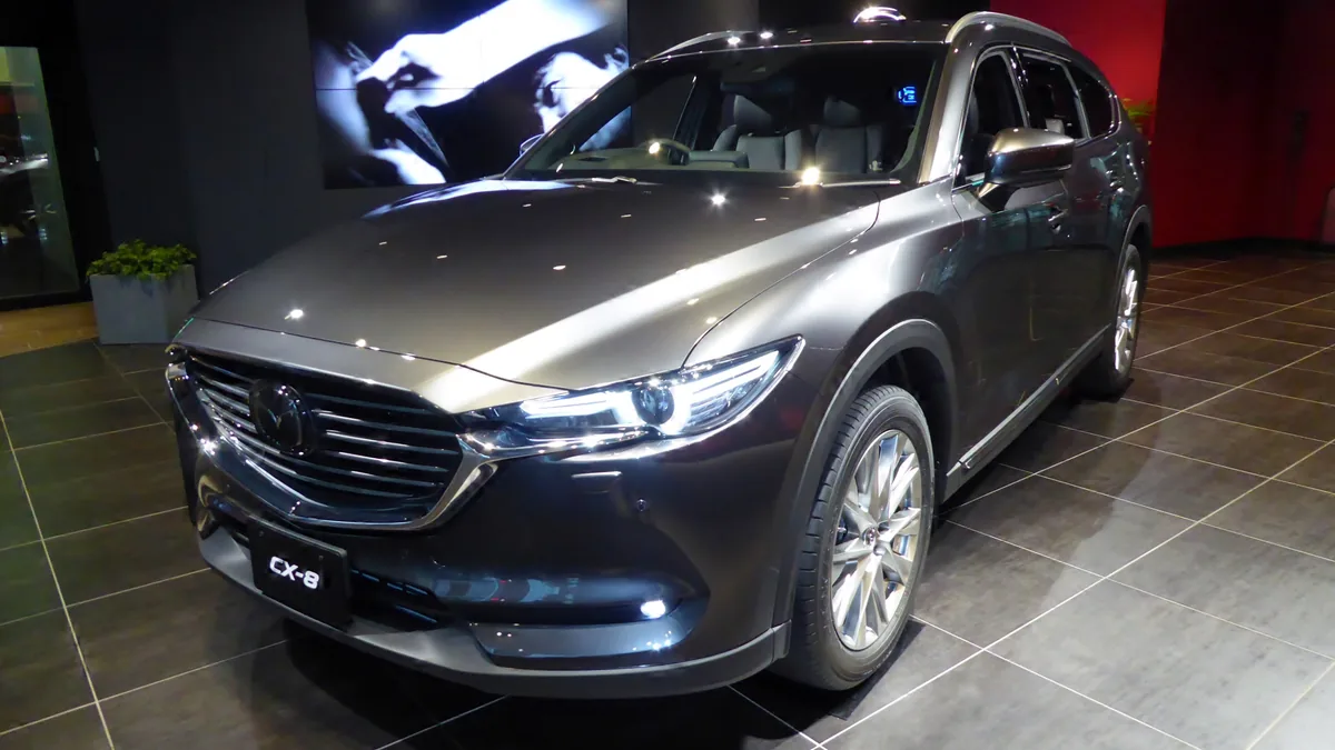 マツダ CX-8（XD L Package）を斜め前から見た写真。ショールームの床に停まるグレーの車体と、大きなグリルが見える
