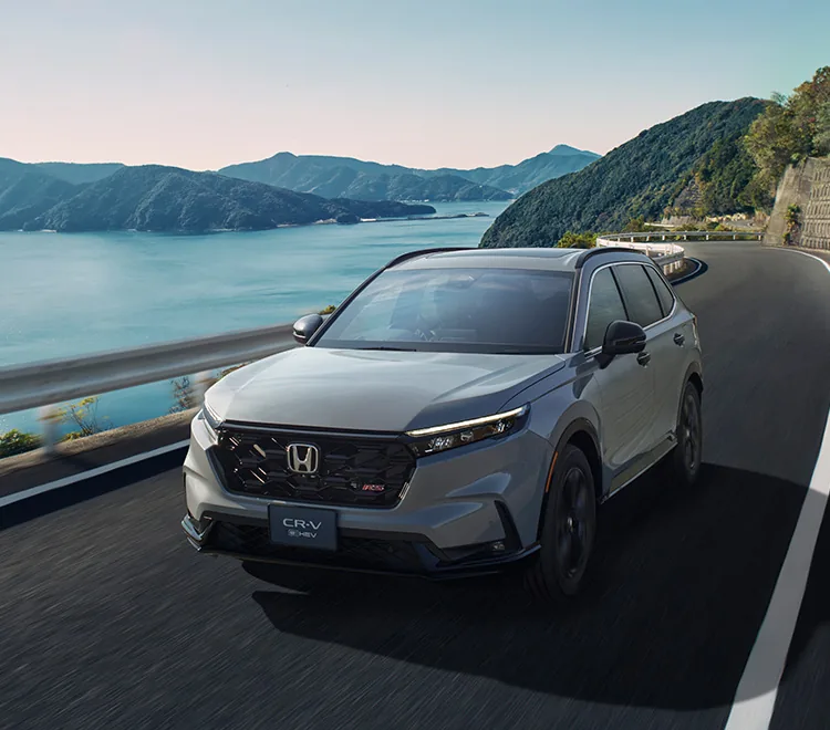 海沿いの山道を走る灰色のCR-V（6代目）。奥に入り江と山が見える