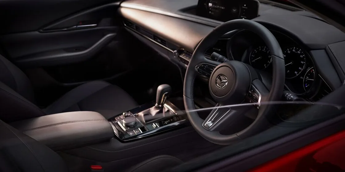 CX-30の運転席まわりを助手席側の斜め後ろから見た様子。暗い室内に、ハンドルとメーター、中央のシフトレバーが浮かぶ