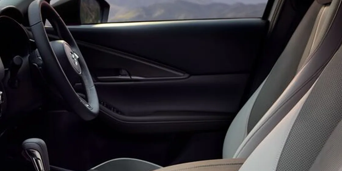 CX-30の運転席のドアの内側とハンドルを、助手席側から見た様子。明るい灰色のシートの奥に、黒いドアの内張りが見える