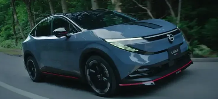 日産リーフ NISMOが木立の中の道を走る外観。灰色がかった青のボディで、フロントバンパーの下と側面の下端に赤い線が入る