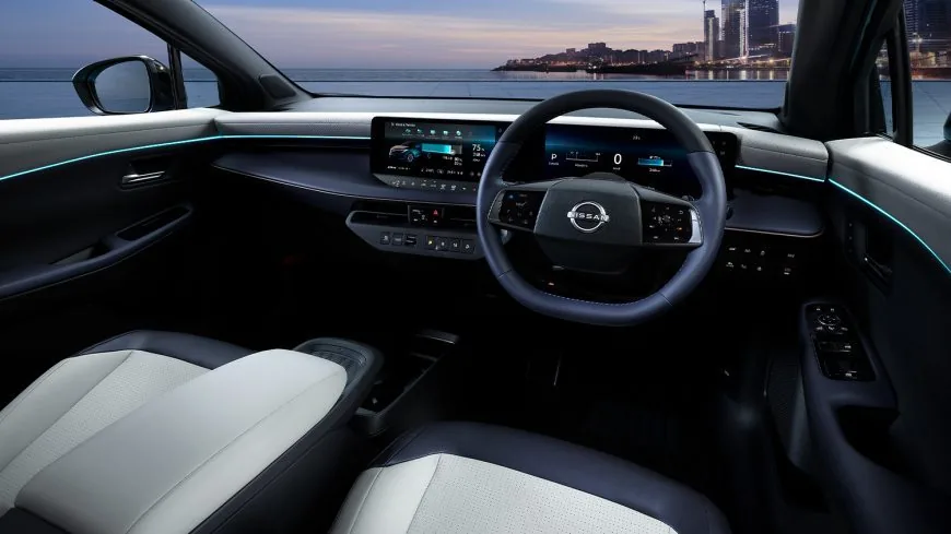 夕方の海辺に止めた日産リーフの運転席まわり。横に長い2つの画面と、ドアからダッシュボードに続く水色の細い照明が見える