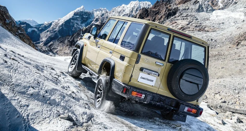 雪の積もった岩山の斜面を登るランドクルーザー70を後ろ斜めから見た外観。背面にスペアタイヤが付いている