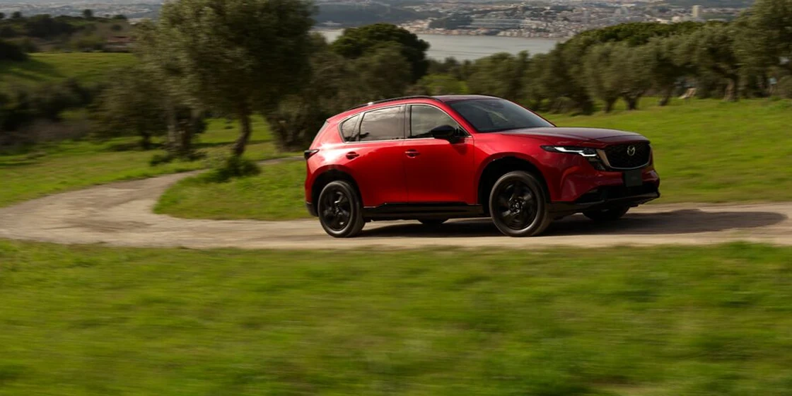 従来型（KF）のCX-5。赤い車が、草地のわきの道を走る外観