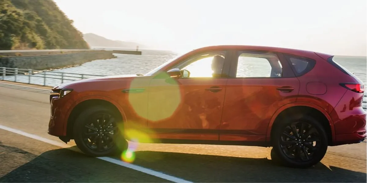 海沿いの道を走る赤いCX-60を真横から見た様子。長い車体の側面と黒いホイールが見える