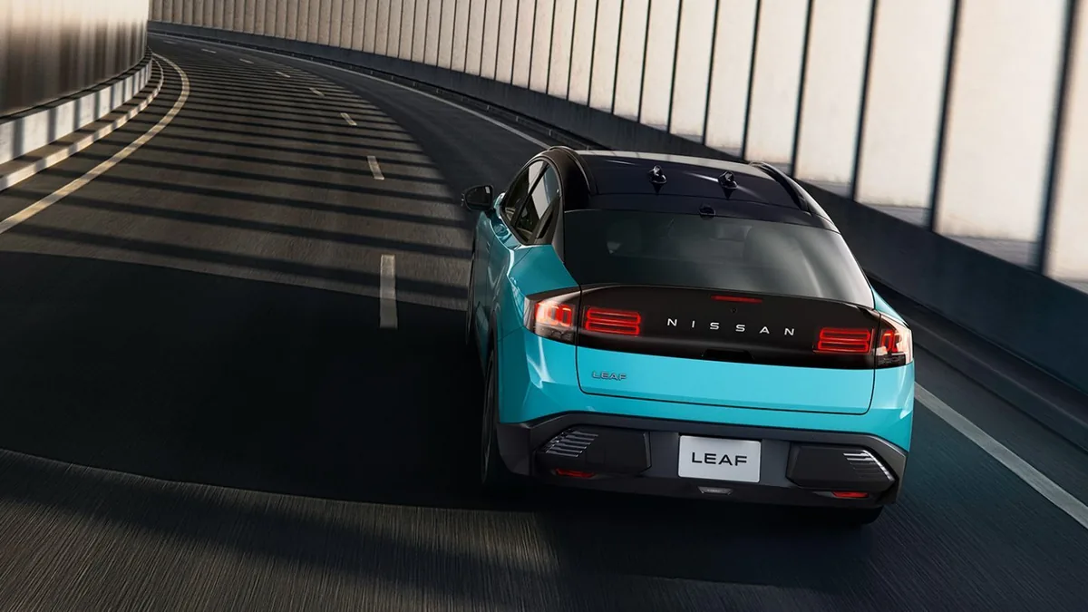 トンネルの中のカーブを走るターコイズの日産リーフを後ろ上から見た外観。横一文字のリアランプの間にNISSANの文字が並ぶ