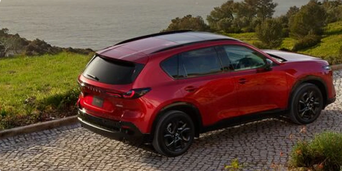 赤い新型CX-5を斜め後ろの上から見た外観。石畳の上に止まり、後ろの窓と細いテールランプが見える