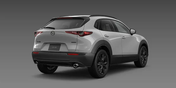 灰色の背景に置いた銀色のCX-30を右斜め後ろから見た外観。黒いホイールと横長のテールランプが分かる