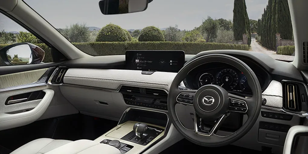 白い内装のCX-80の運転席まわり。横長のディスプレイとハンドル、白い革のシートとドアの内張りが見える