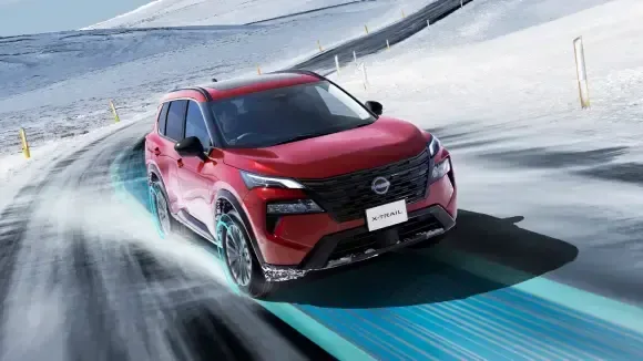 雪の山道のカーブを走る赤い現行エクストレイルを正面から見た画像。車の下に青い光の帯が重ねられている（公式の画像）