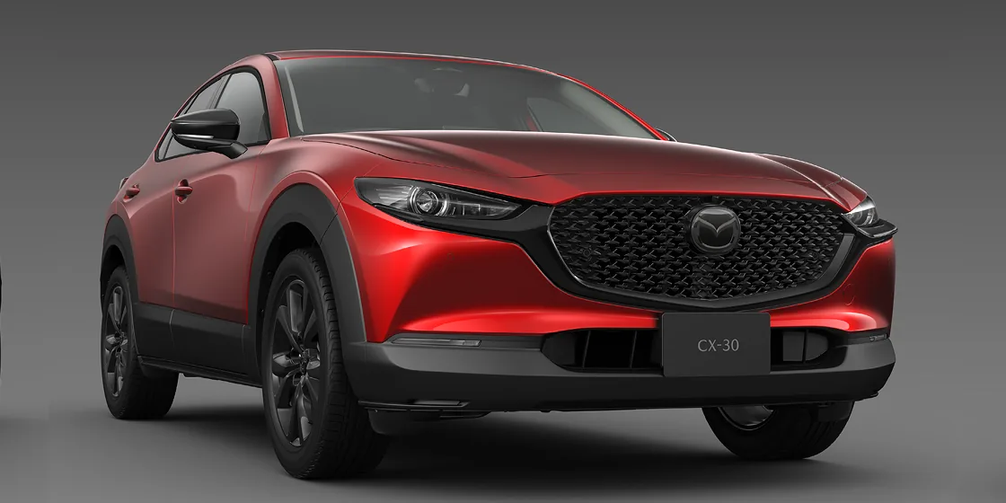 灰色の背景に置いた赤いCX-30を右斜め前から見た外観。大きな黒いグリルと細いヘッドライトが分かる