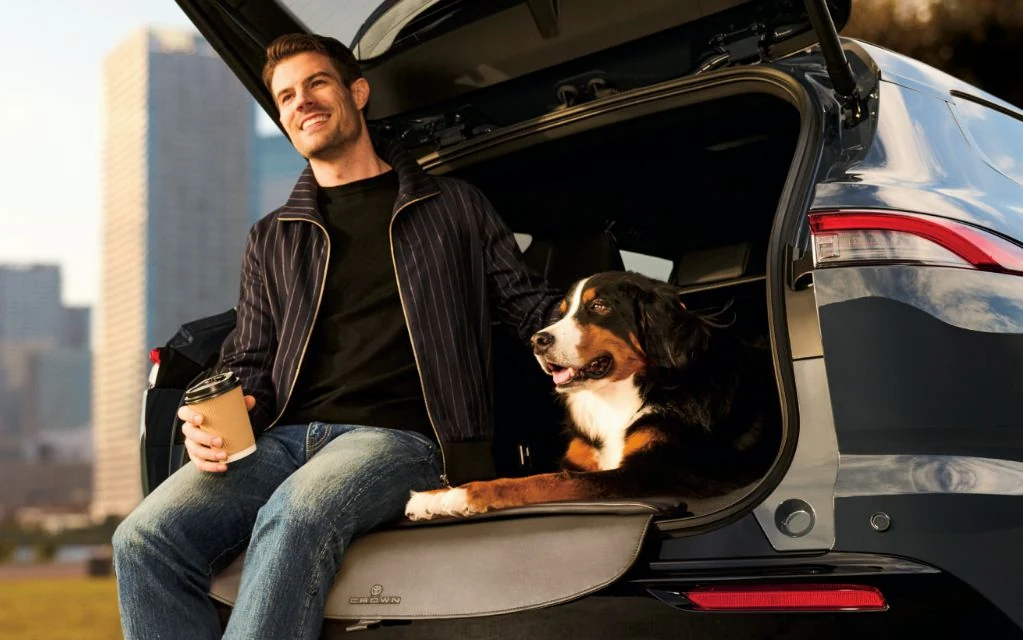 クラウン エステートのバックドアを開けた荷室の端に座る男性と、荷室に乗った犬。後ろに高層ビルがぼんやり見える